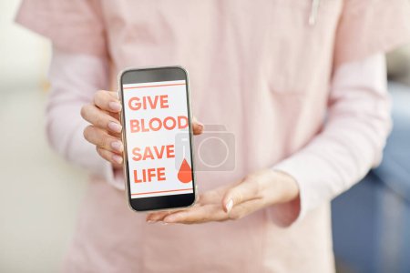 Photo for Close up of female nurse holding smartphone with Give blood save life slogan at blood donation center, copy space - Royalty Free Image