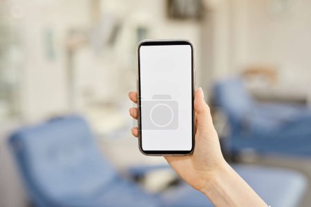 Photo for Close up of female hand holding smartphone with blank screen at blood donation center, copy space - Royalty Free Image
