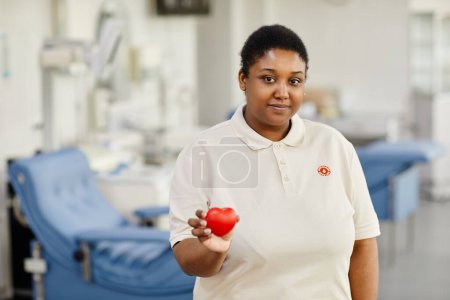 Foto de Retrato de cintura hacia arriba de una joven mujer negra sosteniendo el corazón rojo en el centro de donación de sangre y mirando a la cámara, espacio para copiar - Imagen libre de derechos