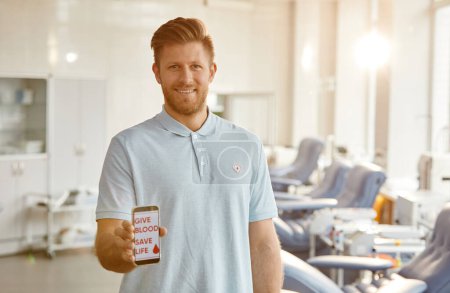 Photo for Minimal waist up portrait of smiling man holding smartphone with Give blood save life slogan at blood donation center, copy space - Royalty Free Image