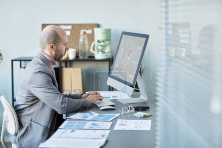 Foto de Retrato de vista lateral mínimo del hombre de negocios maduro que usa la computadora mientras analiza los datos en la oficina de la compañía, espacio de copia - Imagen libre de derechos