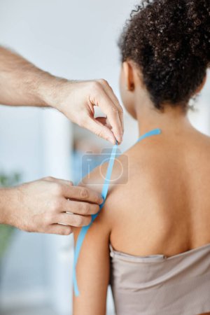 Photo for Close up rehabilitation therapist putting k tape on shoulder of young woman in physiotherapy clinic - Royalty Free Image