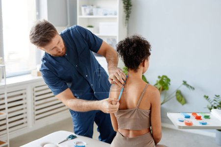 Photo for Portrait of male rehabilitation therapist putting physio tape on shoulder of young woman to relieve muscle pain, copy space - Royalty Free Image