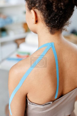 Photo for Vertical closeup of young woman with physio tape on shoulder in rehabilitation therapy - Royalty Free Image