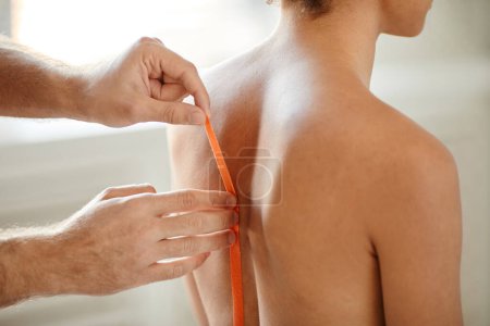 Foto de Primer plano del terapeuta de rehabilitación poner cinta adhesiva en la espalda de la mujer joven para aliviar el dolor muscular, espacio de copia - Imagen libre de derechos