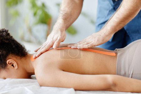 Photo for Closeup of rehabilitation specialist putting physio tape on back of young woman, copy space - Royalty Free Image