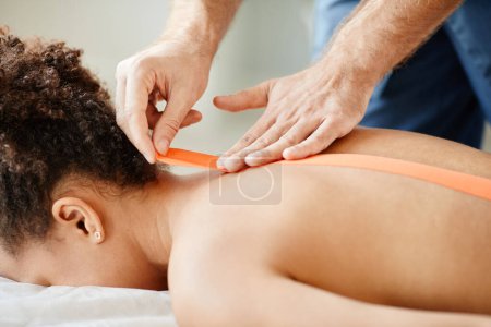 Photo for Close up of male rehabilitation specialist putting physio tape on back of young woman, copy space - Royalty Free Image