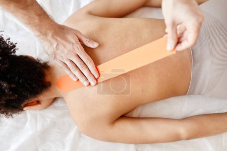 Photo for Top down view of rehabilitation therapist putting physio tape on back of young woman, copy space - Royalty Free Image