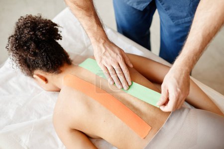 Photo for Top view of male rehabilitation specialist putting physio tape on back of young woman, copy space - Royalty Free Image