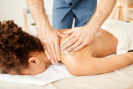 Téléchargez les photos : Gros plan de l'esthéticienne masculine donnant massage de dos à la jeune femme afro-américaine profitant de la session SPA - en image libre de droit
