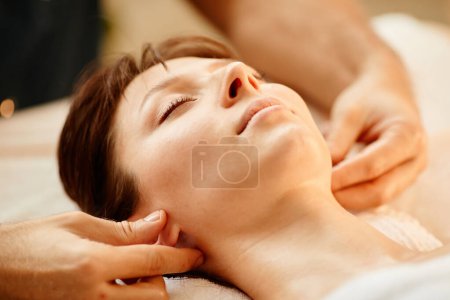 Foto de Primer plano de hermosa chica disfrutando de la sesión de masaje facial en el centro de SPA con los ojos cerrados - Imagen libre de derechos