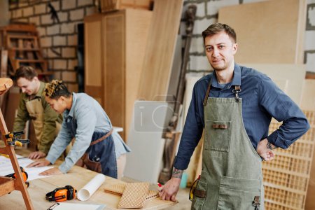Téléchargez les photos : Portrait chaleureux de charpentier masculin souriant regardant la caméra tout en restant debout dans un atelier artisanal, espace de copie - en image libre de droit