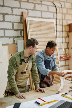 Photo for Vertical portrait of two carpenters designing handcrafted furniture piece in workshop - Royalty Free Image