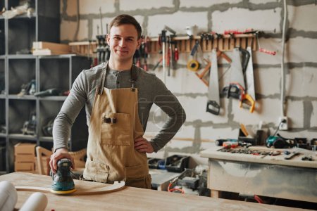 Photo for Warm toned shot of young carpenter smiling at camera while building furniture in workshop, copy space - Royalty Free Image