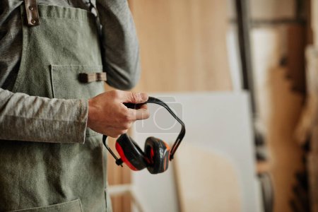 Foto de Primer plano del trabajador que sostiene auriculares de cancelación de ruido en taller, producción y seguridad, espacio para copias - Imagen libre de derechos