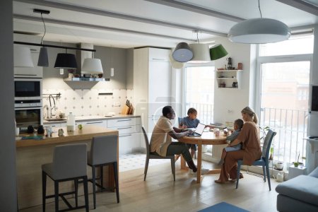 Foto de Amplia escena del hogar del ángulo de la familia multiétnica moderna en la mesa de la cena en la cocina, espacio de copia - Imagen libre de derechos