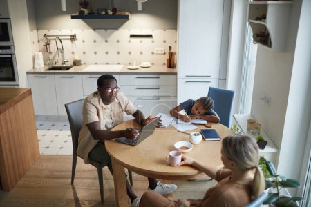 Téléchargez les photos : Scène de maison en angle élevé de la famille multiethnique moderne à table dans la cuisine, espace de copie - en image libre de droit