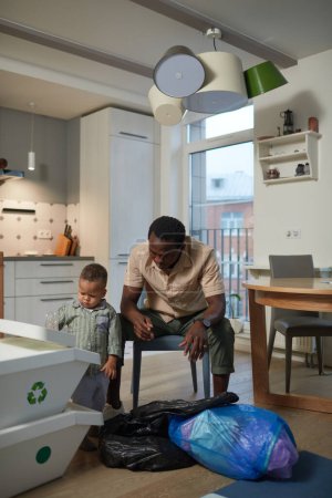 Photo for Vertical portrait of caring black father with baby son sorting plastic waste in kitchen - Royalty Free Image