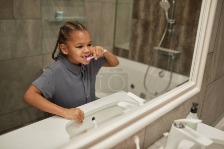 Foto de Espejo retrato de linda chica negra cepillándose los dientes con cepillo de dientes rosa buena práctica de higiene dental en la infancia - Imagen libre de derechos