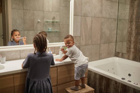 Téléchargez les photos : Portrait de deux enfants afro-américains dans la salle de bain accent sur petit garçon brossant les dents, espace de copie - en image libre de droit