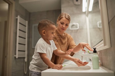 Foto de Retrato de madre joven ayudando a un niño lindo a cepillarse los dientes en el baño, espacio para copiar - Imagen libre de derechos