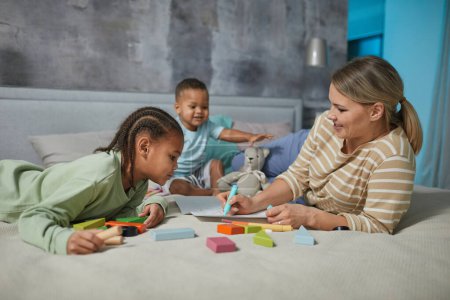 Photo for Portrait of happy Caucasian mother with two African American children playing on bed together - Royalty Free Image
