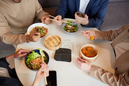 Foto de Vista superior en grupo de cuatro personas disfrutando de varios alimentos asiáticos en la mesa redonda durante el almuerzo de negocios en la cafetería - Imagen libre de derechos