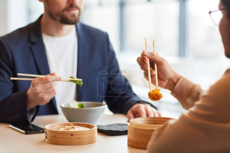 Téléchargez les photos : Gros plan de l'homme d'affaires profitant de la nourriture asiatique pendant le déjeuner d'affaires avec un collègue au café, espace de copie - en image libre de droit