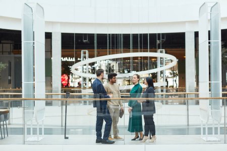 Photo for Wide angle view at diverse group of business people chatting while standing in center of glass office building, copy space - Royalty Free Image