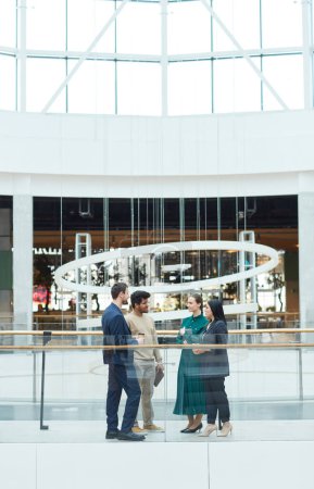 Foto de Vista vertical de gran angular en el diverso grupo de gente de negocios charlando mientras está de pie en el centro del edificio de oficinas de vidrio - Imagen libre de derechos