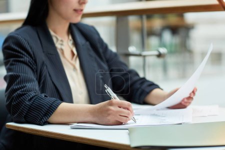 Photo for Close up of young businesswoman writing in document while working at cafe table in office building setting, copy space - Royalty Free Image