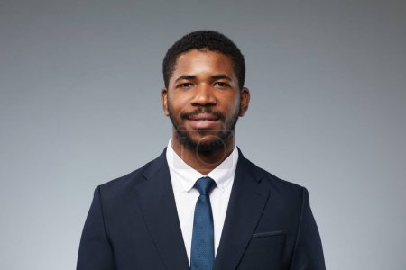 Téléchargez les photos : Portrait de l'homme noir adulte portant un costume d'affaires et souriant à la caméra sur fond gris uni - en image libre de droit