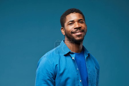 Photo for Portrait of smiling African American man wearing blue on blue background and looking at camera, copy space - Royalty Free Image