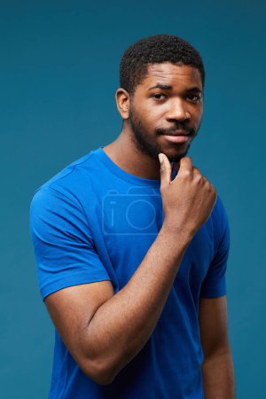 Foto de Retrato vertical del hombre negro guapo mirando a la cámara con presumido mientras usa azul sobre fondo azul - Imagen libre de derechos