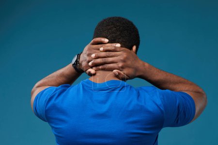 Foto de Vista posterior del hombre negro musculoso con las manos en el cuello usando azul contra el fondo azul vibrante - Imagen libre de derechos