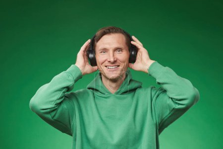Foto de Retrato de la cintura hacia arriba del hombre adulto sonriente que usa auriculares y sudadera verde sobre un fondo verde vibrante, espacio para copiar - Imagen libre de derechos