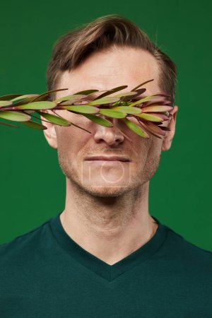 Foto de Retrato vertical de primer plano del hombre caucásico con ojos que cubren las plantas sobre un fondo verde vibrante - Imagen libre de derechos