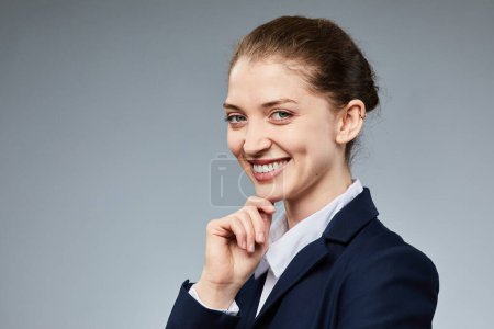 Photo for Portrait of smiling young businesswoman looking at camera while standing against grey background in studio, copy space - Royalty Free Image