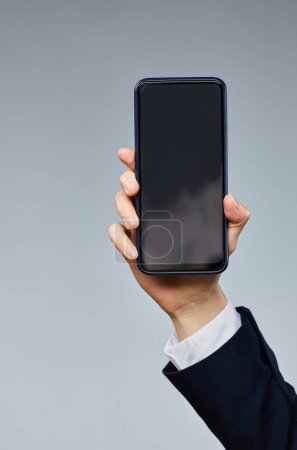 Foto de Primer plano de la mano femenina que sostiene el teléfono inteligente con la pantalla en blanco a la cámara contra el fondo gris - Imagen libre de derechos
