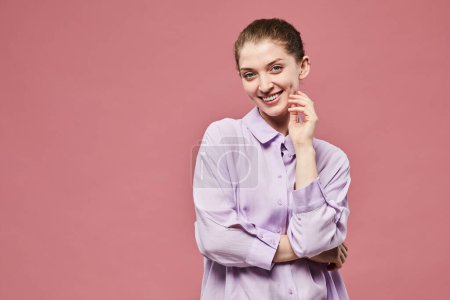 Foto de Retrato de cintura hacia arriba de una joven sonriente de pie sobre un vibrante fondo rosa en el estudio con una manera lúdica, espacio para copiar - Imagen libre de derechos