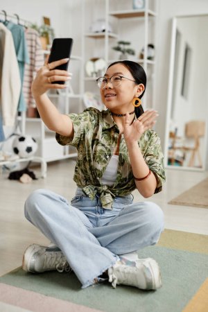 Foto de Retrato vertical de larga duración de una joven adolescente filmando una historia para redes sociales mientras está sentada en el suelo en casa - Imagen libre de derechos