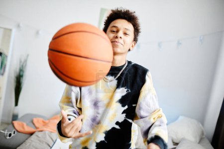 Photo for Waist up portrait of young teenage boy playing with basketball ball at home and smiling to camera - Royalty Free Image