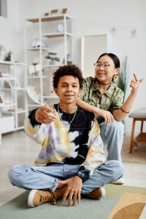 Foto de Retrato vertical de larga duración de dos adolescentes de la generación Z niño y niña sonriendo a la cámara mientras posan en el interior del hogar - Imagen libre de derechos