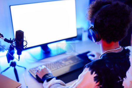 Téléchargez les photos : Gros plan d'un adolescent jouant à un jeu vidéo et diffusant en direct en néon bleu avec maquette d'écran blanc, espace de copie - en image libre de droit