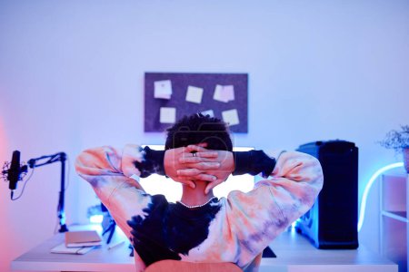 Téléchargez les photos : Vue arrière de adolescent garçon regarder des vidéos sur PC la nuit avec néon bleu, espace de copie - en image libre de droit