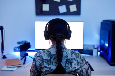 Photo for Back view of teenage girl playing video games at night with blue neon lighting, copy space - Royalty Free Image