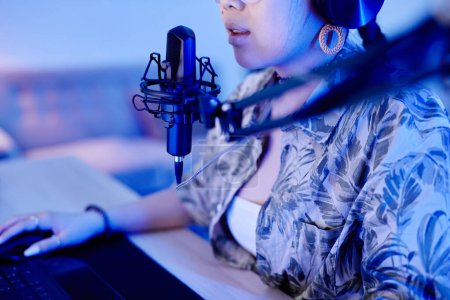 Téléchargez les photos : Gros plan de jeune adolescente jouant à un jeu vidéo sur PC et parlant au microphone tout en streaming en direct dans la lumière bleue néon - en image libre de droit