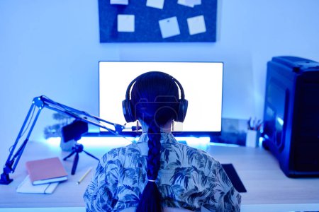 Photo for Back view of teenage girl recording podcast at night with blue neon lighting, copy space - Royalty Free Image