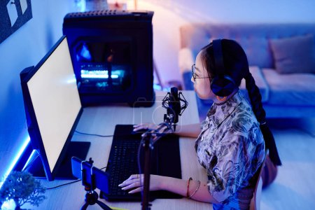 Téléchargez les photos : Portrait grand angle de jeune adolescente enregistrant podcast la nuit avec éclairage au néon bleu, espace de copie - en image libre de droit
