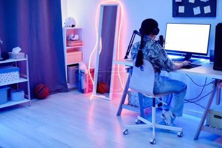 Photo for Wide angle angle portrait of young teenage girl recording podcast at night in room with blue neon lighting, copy space - Royalty Free Image